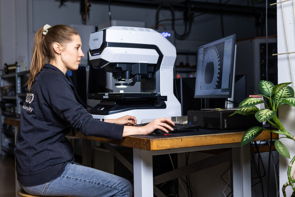 Fachkraft prüft ein mikrogefertigtes Teil unter dem Mikroskop zur Qualitätssicherung nach ISO 13485.